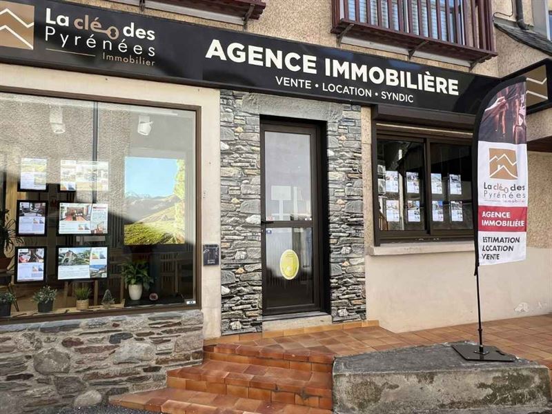 Vitrine de l'agence immobilière La Clé des Pyrénées, façade en pierre et annonces en vitrine